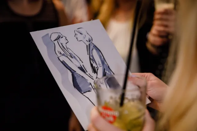 Person holding drink and looking at caricature sketch by Björn von Schlippe