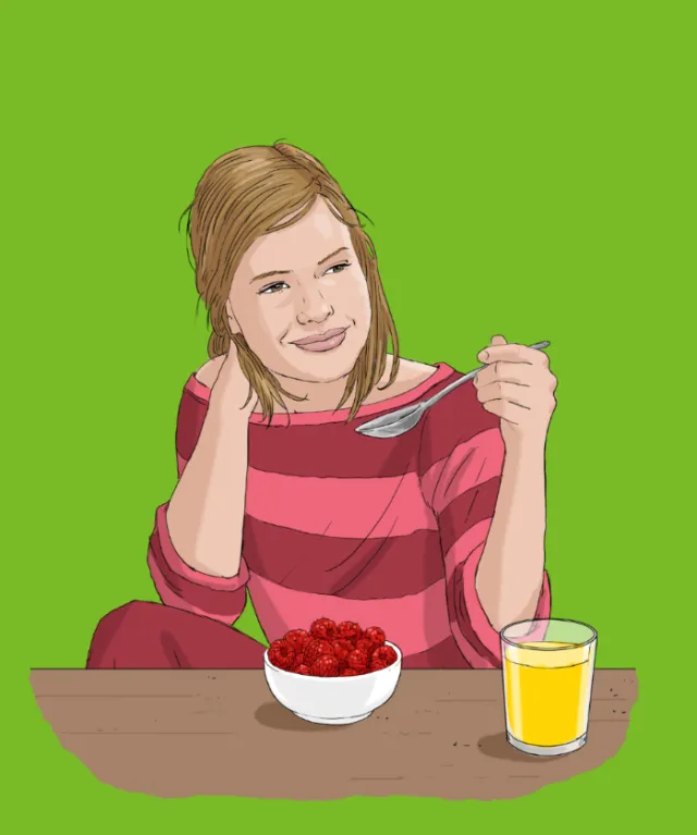 Woman eating raspberries from a bowl with a glass of juice by Andreas Schickert