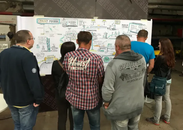 Five people studying a large detailed diagram on a wall by Björn von Schlippe