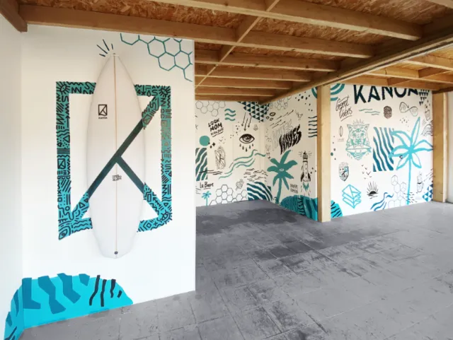 Surfboard mounted on patterned wall with wooden ceiling beams by Andy Gellenberg