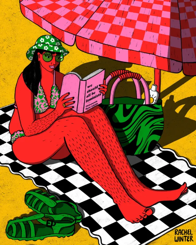 Woman reading book on beach towel under umbrella by Rachel Winter