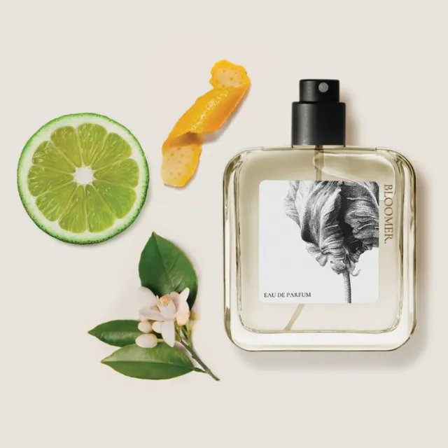 Perfume bottle with citrus slice, orange peel, and flowers by Reiko Lauper