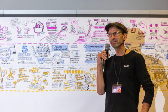Man with microphone presenting in front of whiteboard covered with sketches