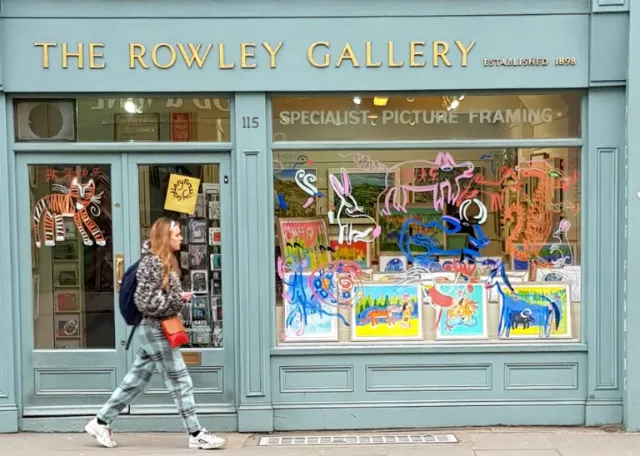 The Rowley Gallery shopfront with vibrant framed pictures and neon art in window.