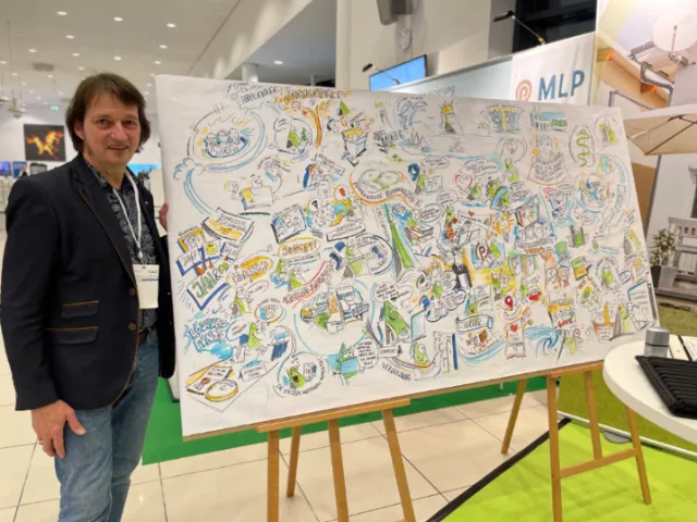 Person standing beside a large illustrated whiteboard on an easel at an event