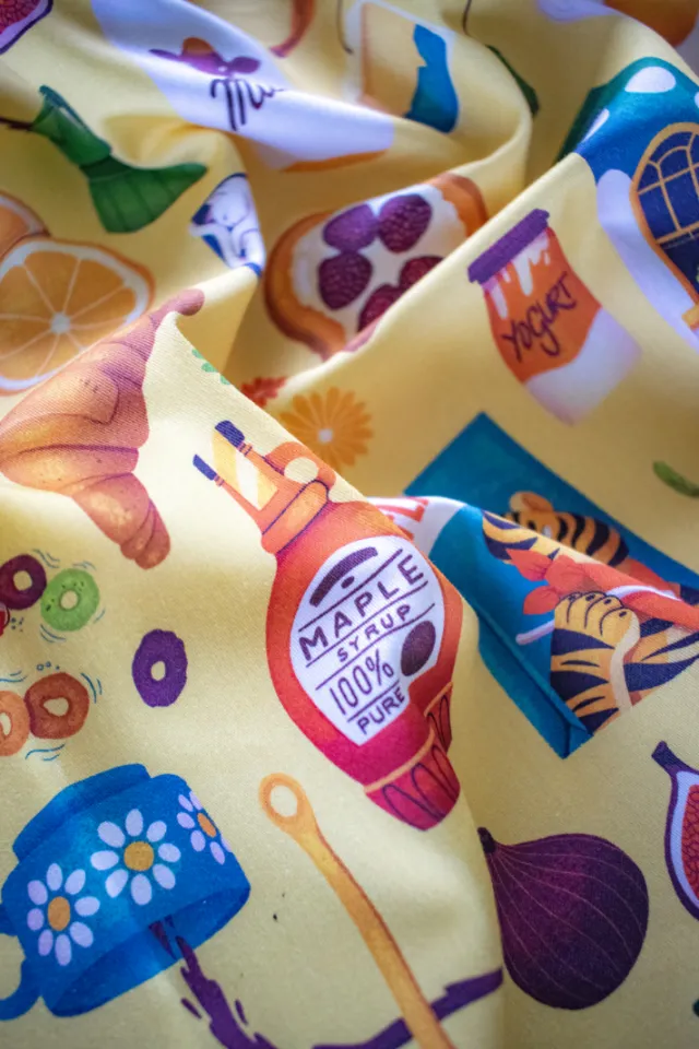 Fabric with illustrations of croissant, maple syrup, honey, and fruits.