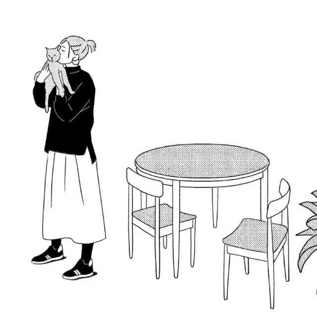 Woman in black sweater holding a cat beside dining table with two chairs