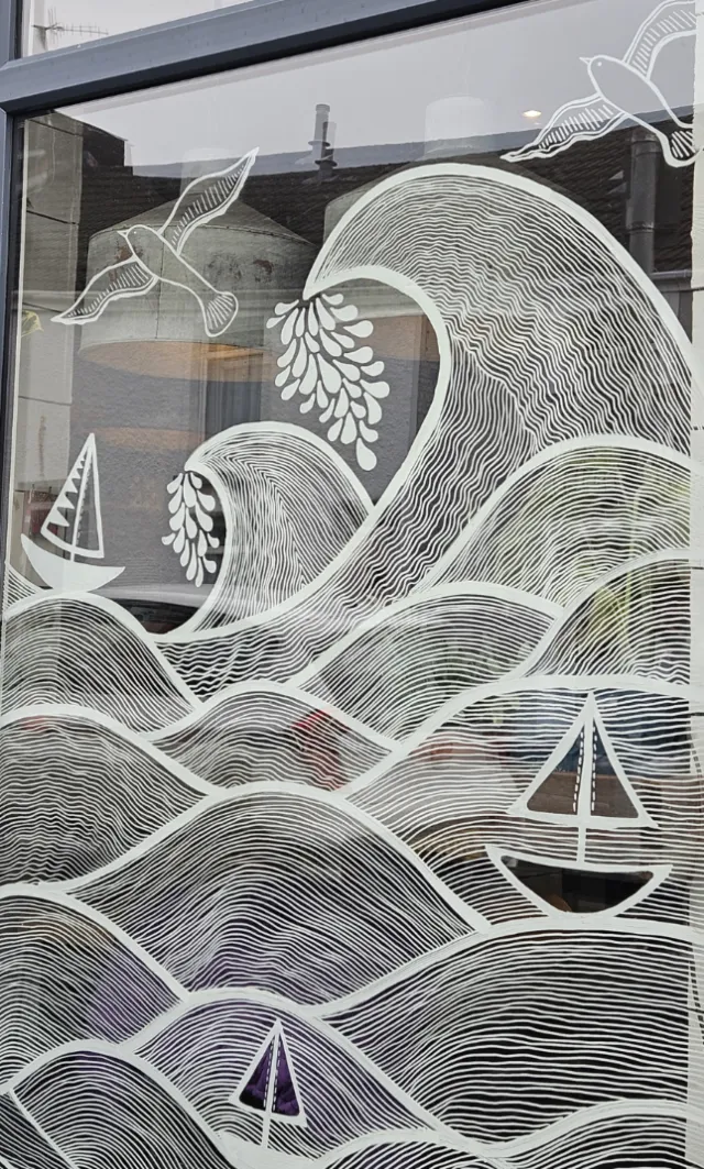 White line art mural of waves, birds and sailboats on window