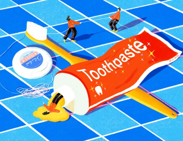 Miniature people cleaning giant toothbrush and toothpaste on blue tiles