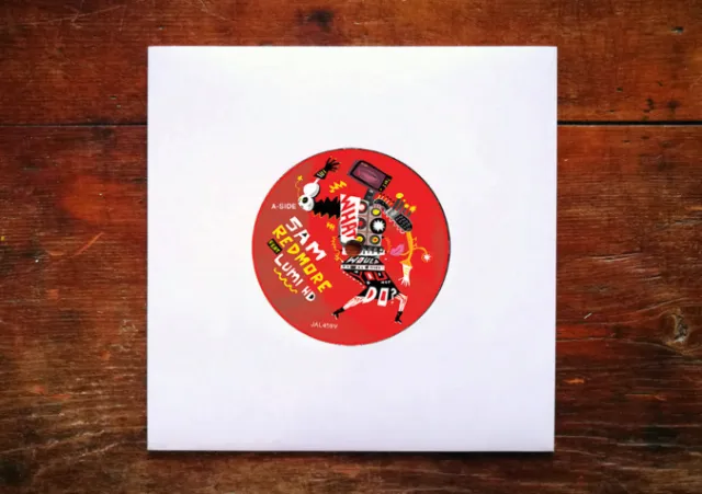 Vinyl record with red label on wooden surface in white sleeve