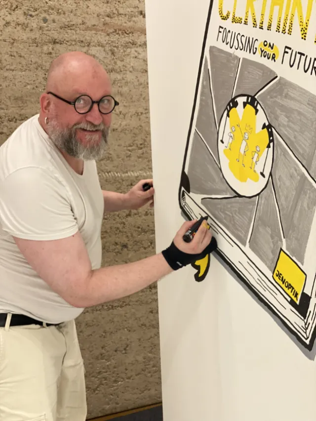 Man in white shirt drawing a black and yellow illustration on wall