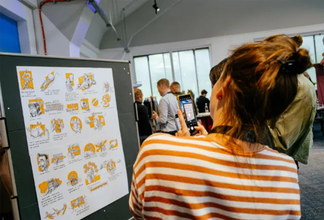 Woman taking photo of illustrated posters at indoor exhibition