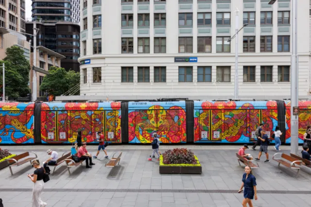 Brightly painted tram in city plaza with people walking nearby