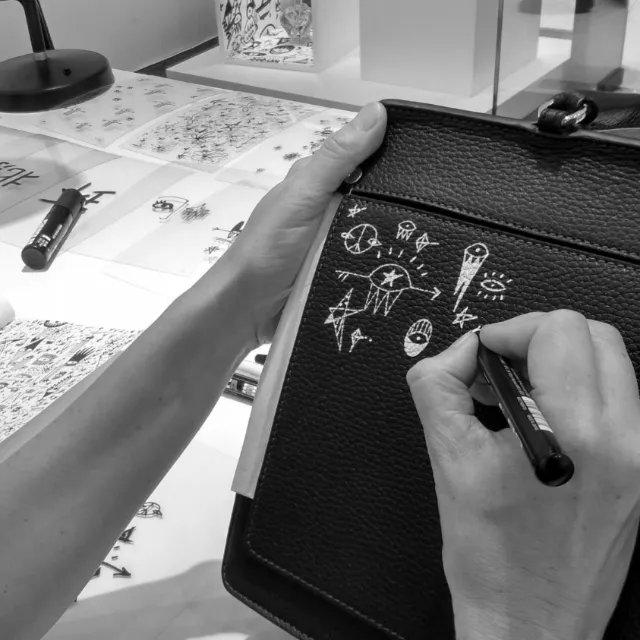 Hands creating white abstract doodles on black leather with marker