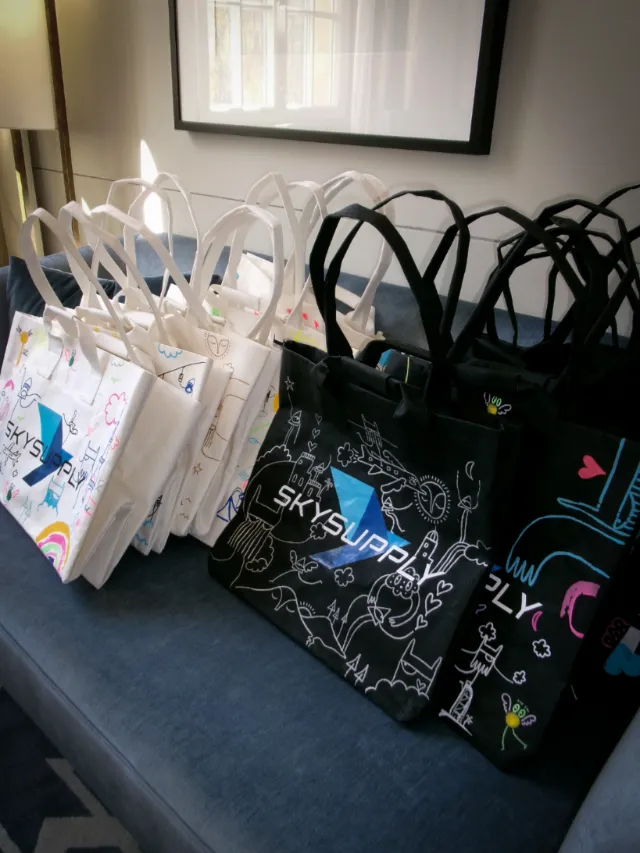 Rows of white and black reusable tote bags with colorful abstract patterns