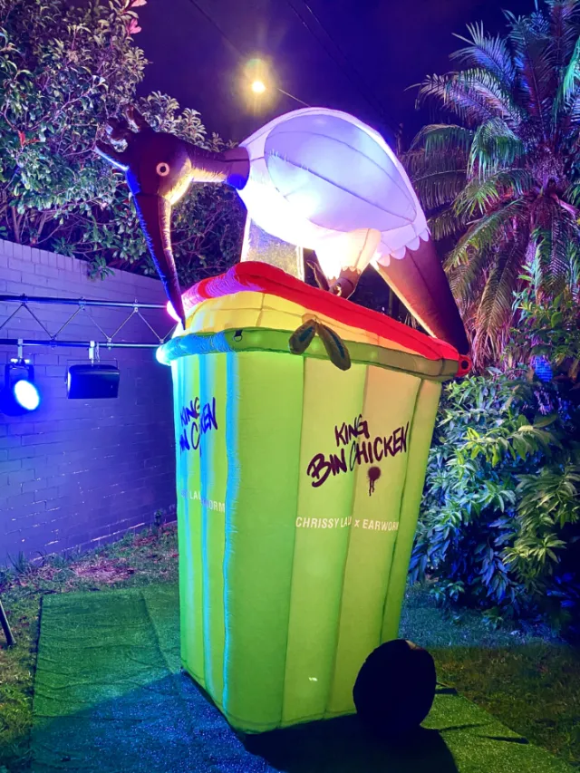 Brightly lit bird sculpture on green trash bin outdoors at night