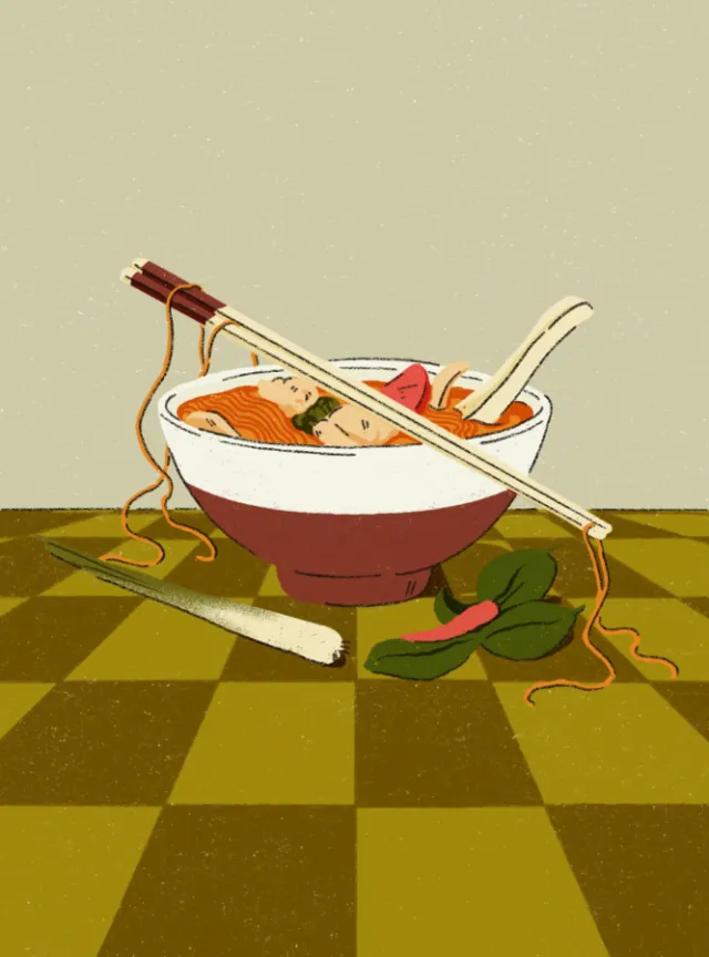 Bowl of noodle soup with chopsticks, spoon, and vegetables on checkered surface