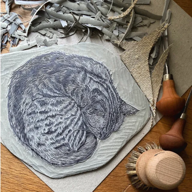 Lino block print of sleeping cat with carving tools by Emily Robertson