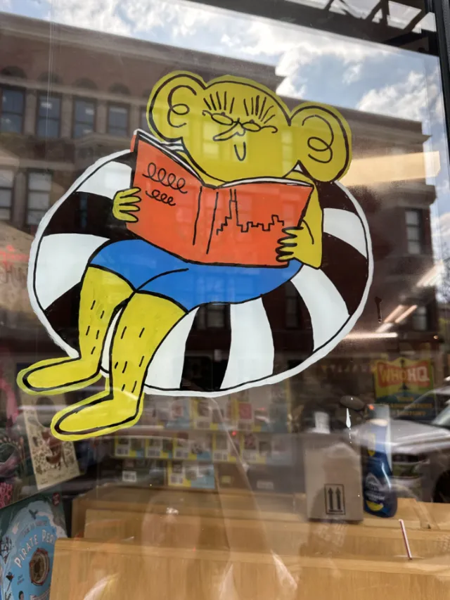 Cartoon character reading book in bookstore window by Ollie Wootton