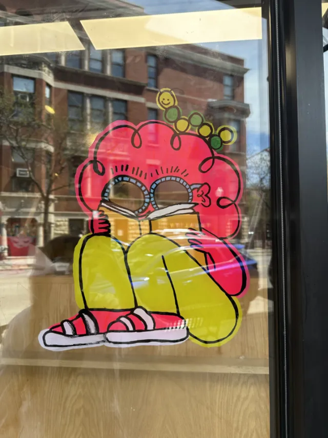 Cartoon character with red hair and sunglasses painted on window by Ollie Wootton