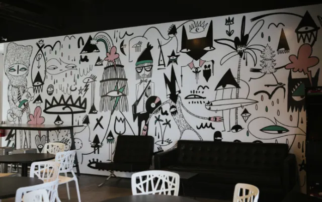 Black and white abstract mural in cafe with black sofa and white chairs by Nadia Flower