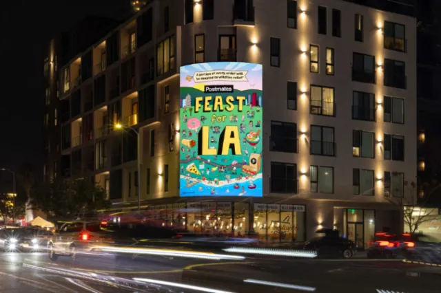 Daniel Sulzberg’s Feast LA poster illuminated on a city building at night