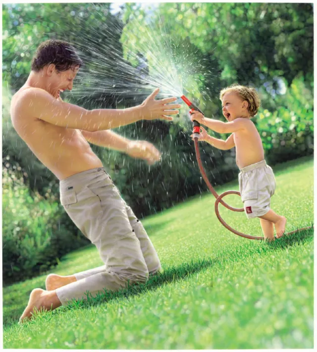 Child spraying water from garden hose at smiling man by Tom Ungemach